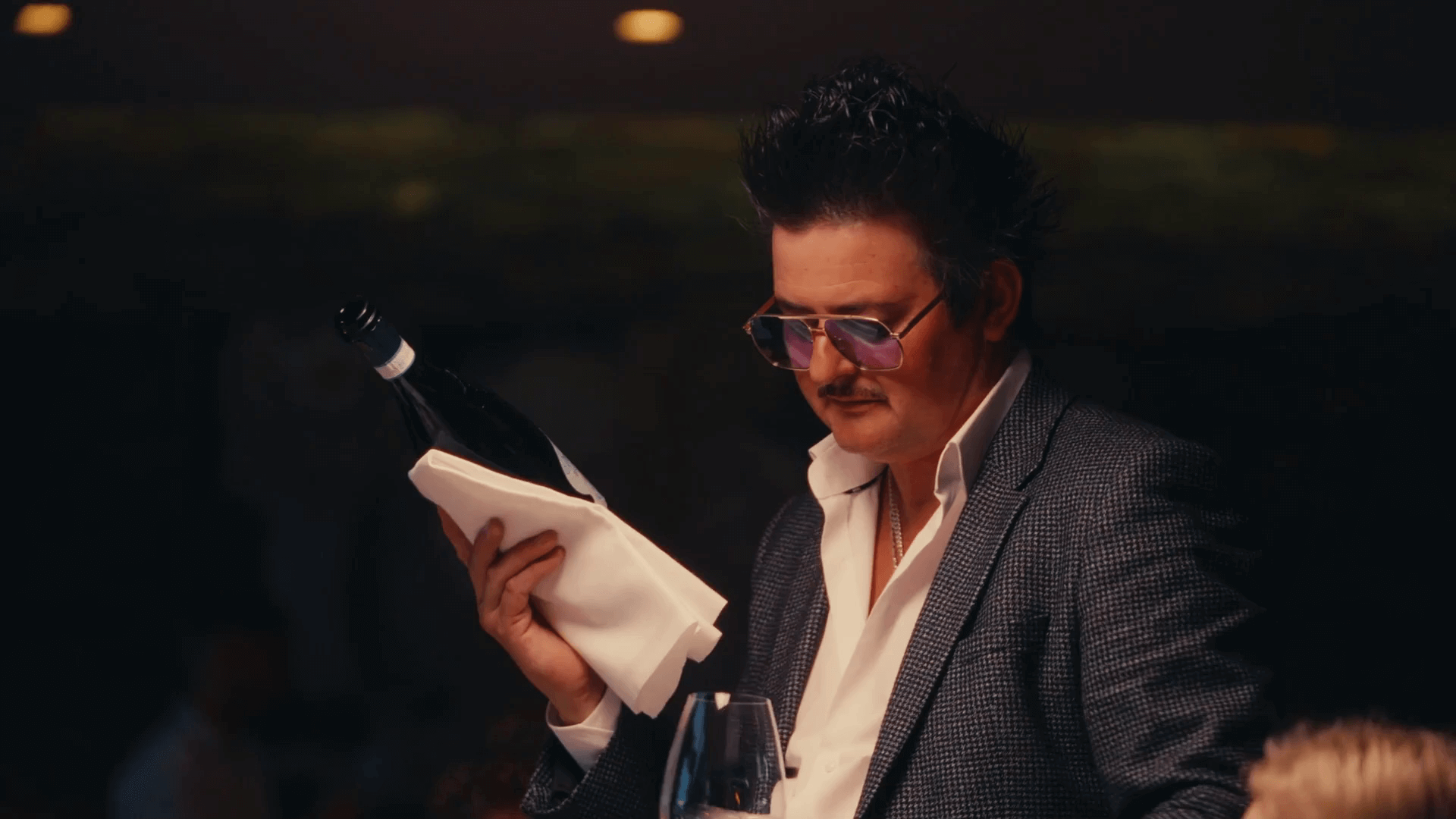 Der Sommelier hat eine edle Flasche Wein in der rechten Hand, in der linken ein Weinglas.