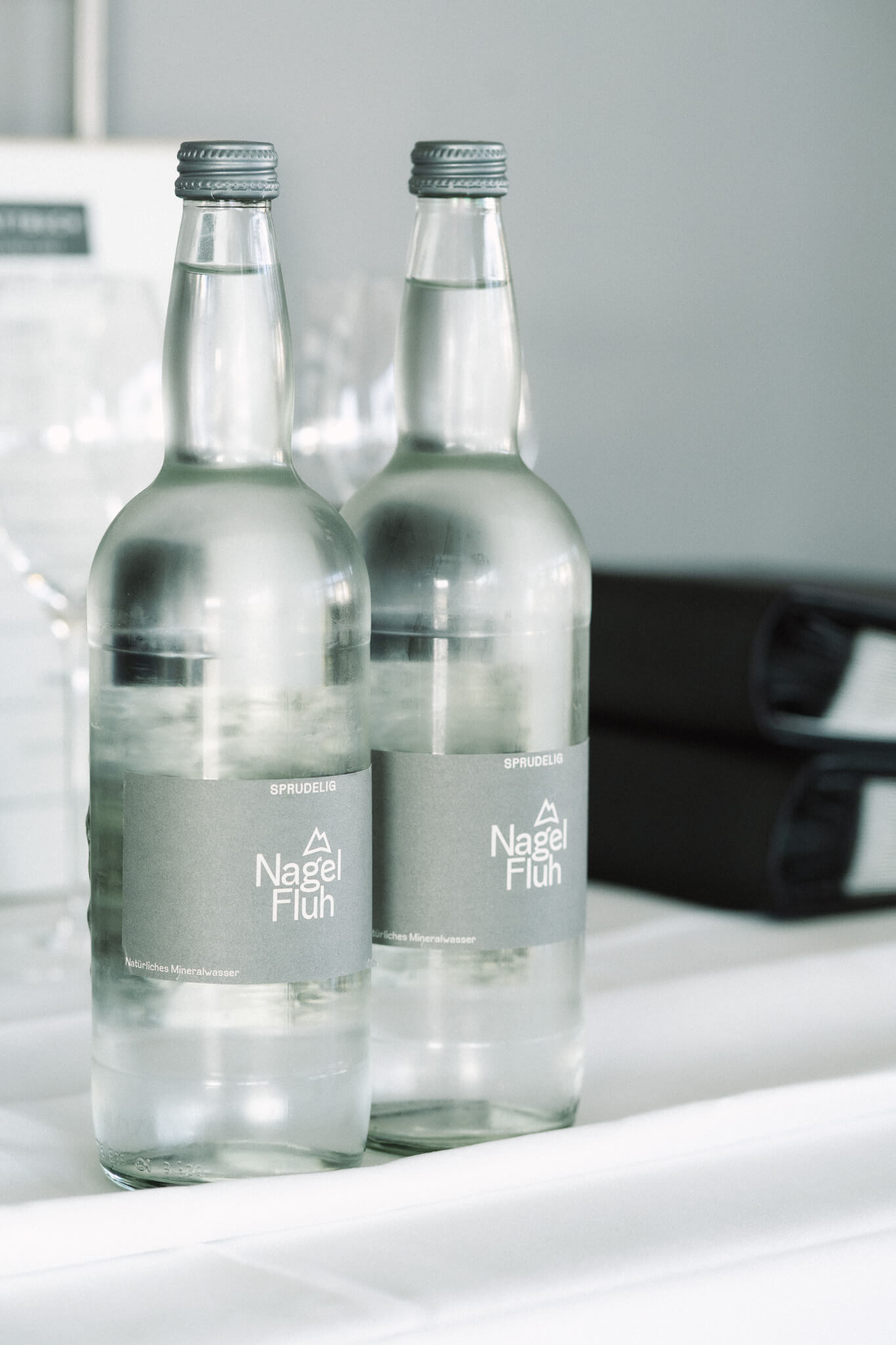 Zwei Wasserflaschen mit der Aufschrift "Nagelfluh" nebeneinander auf einer weißen Tischdecke