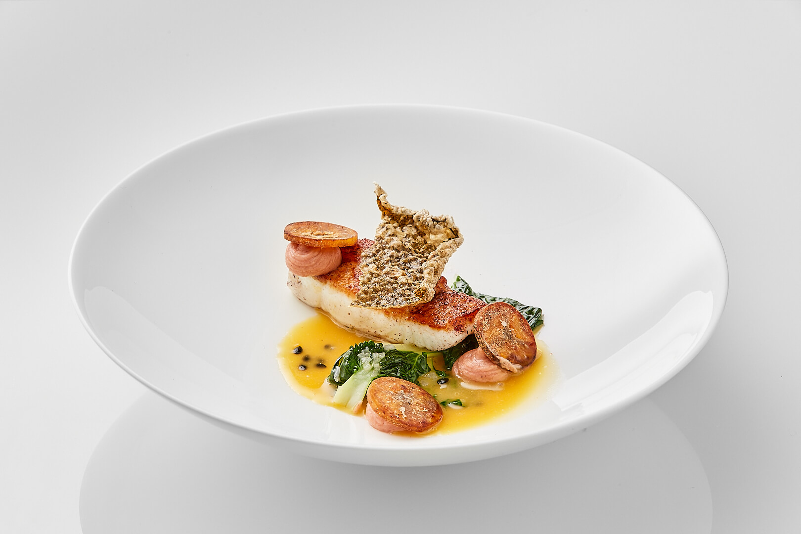 Weißer Teller mit einem Fischgericht, Sauce und Beilagen