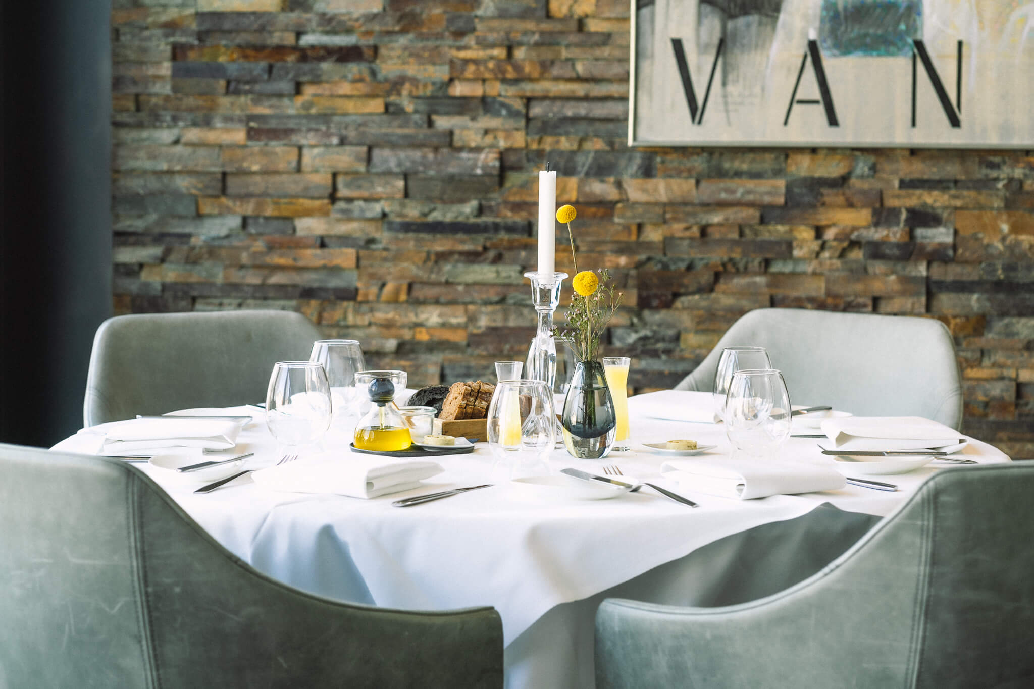 Eingedeckter Tisch mit Blumen, Gläsern und einer Steinwand im Hintergrund, die ein Gemälde schmückt