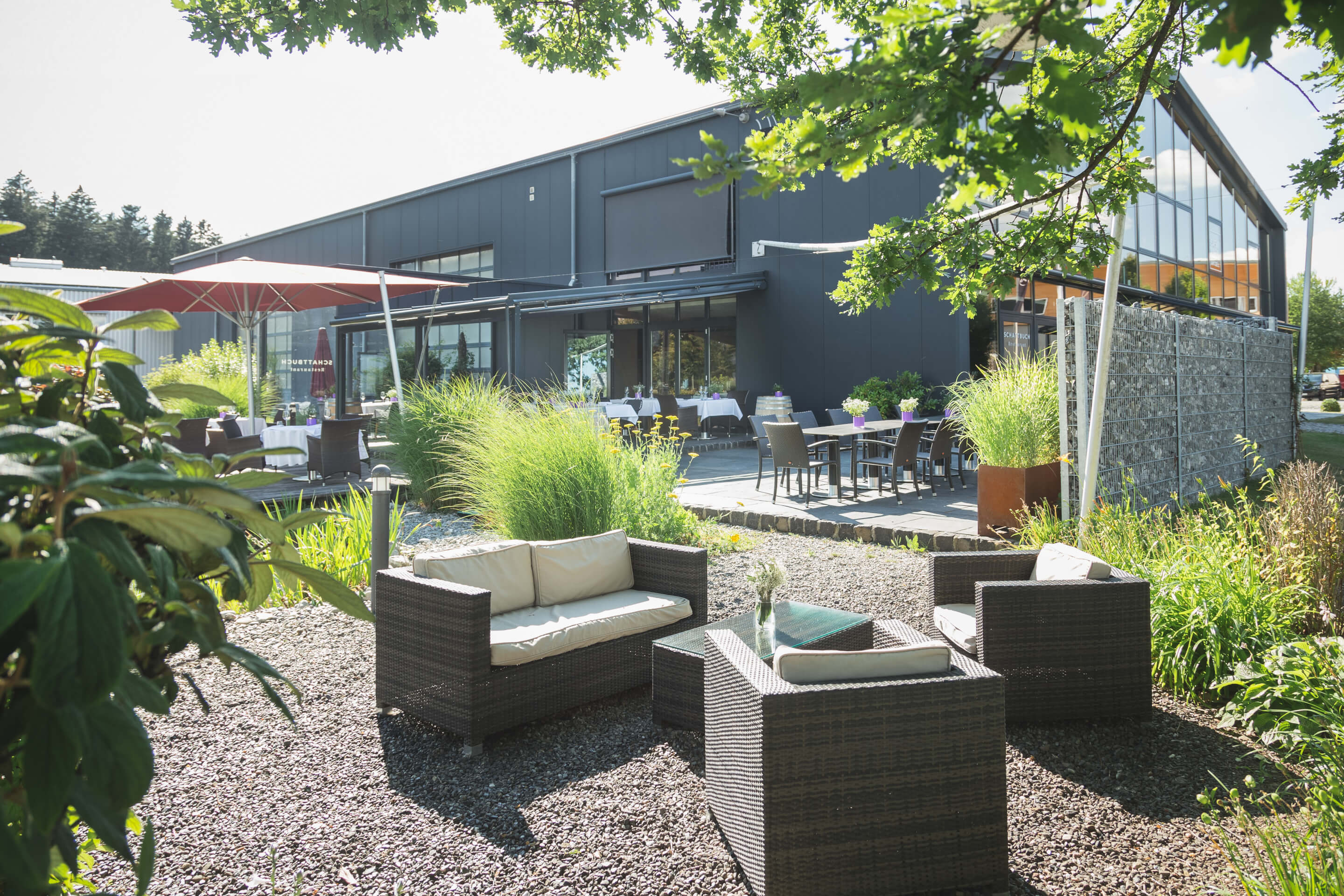 Loungemöbel und Gartenmöbel vor einem Gebäude mit Gräsern und Bäumen