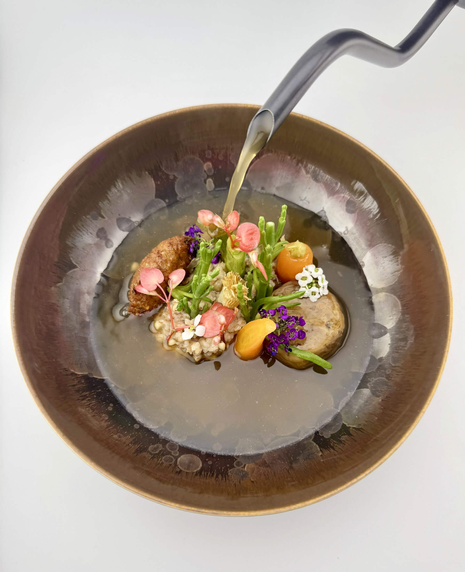 Tiefer strukturierter Teller mit Brühe Lauchessenz und Fleisch sowie Blüten