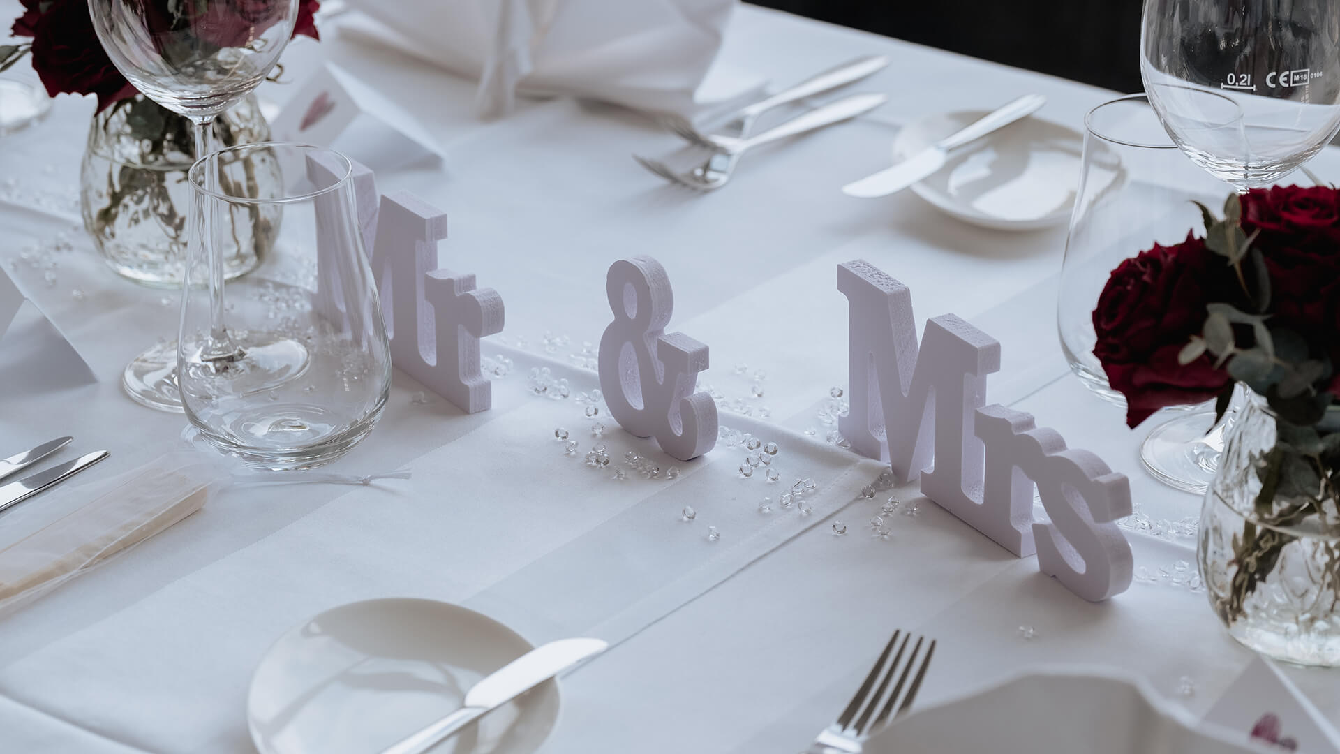 Tischdekoration mit Mr & Mrs Buchstaben auf dem Tisch neben Besteck, Tellern und Gläser sowie Blumen