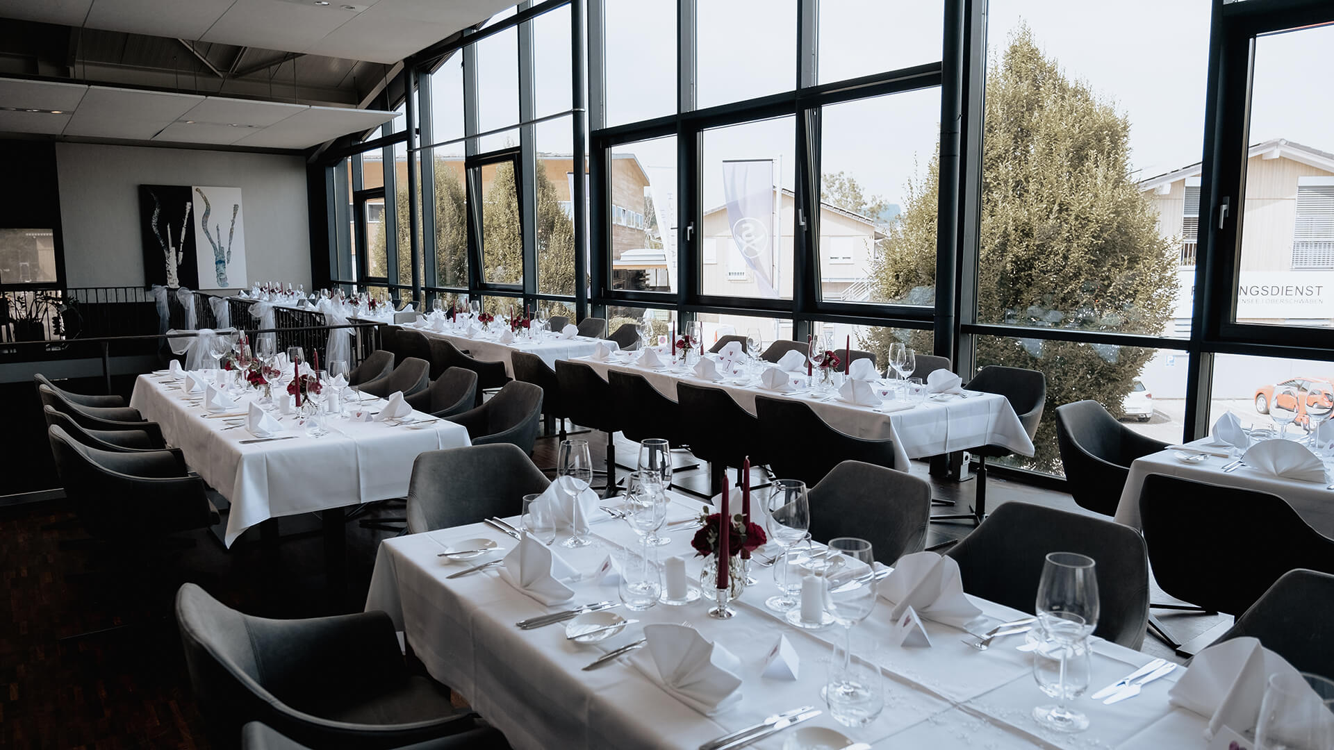 Lange weiß eingedeckte Tafeln mit Gedeck und Servietten in einem lichtdurchfluteten Eventraum