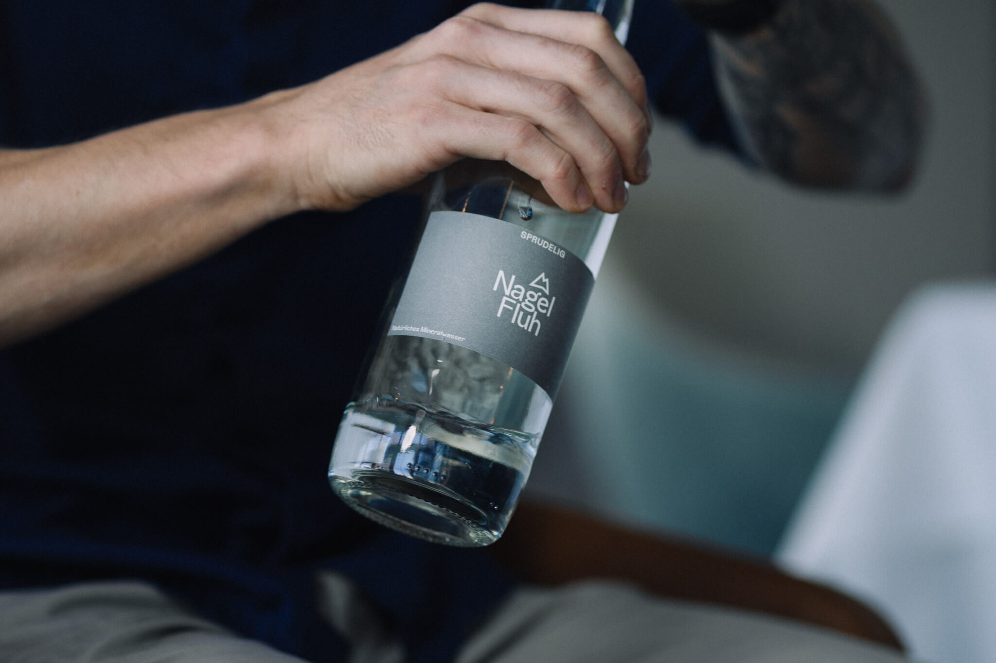 Ein Mann hält eine edle Flasche Allgäuer Alpenwasser in der Hand. Kooperation zwischen dem Allgäuer Alpenwasser und dem Restaurant Schattbuch.