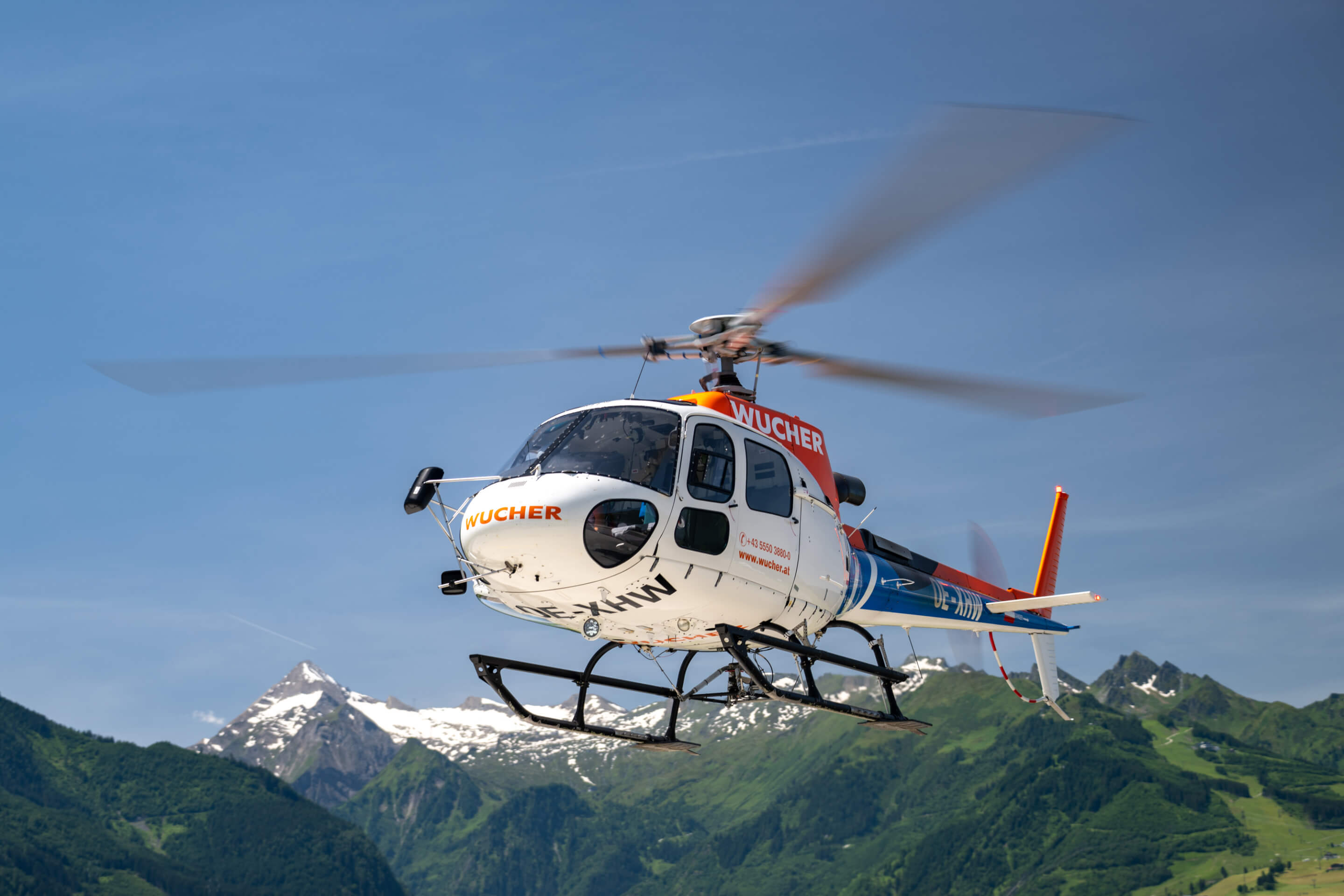 Ein weiß-oranger Hubschrauber mit rotierenden Rotorblättern vor beeindruckender Bergkulisse